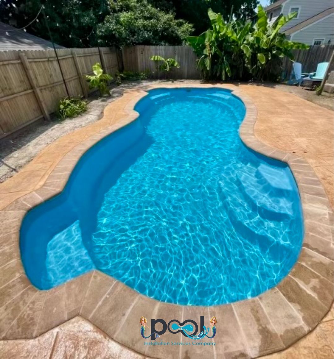 Blue swimming pool with light brown stone edge in a backyard with a fence.