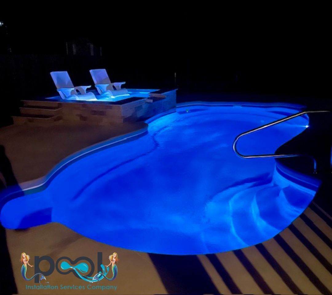 Blue illuminated pool at night with two lounge chairs on the side.