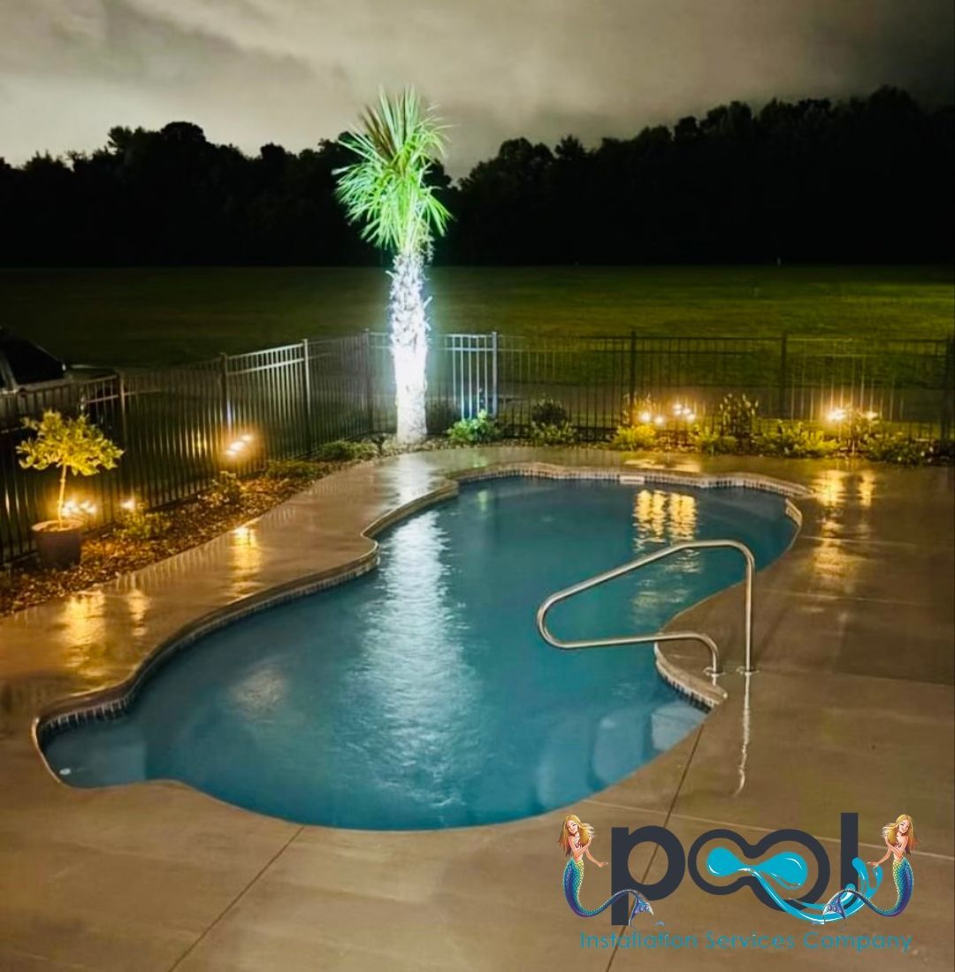 Night view of a kidney-shaped pool with a palm tree, lit by lights, reflecting on the water.