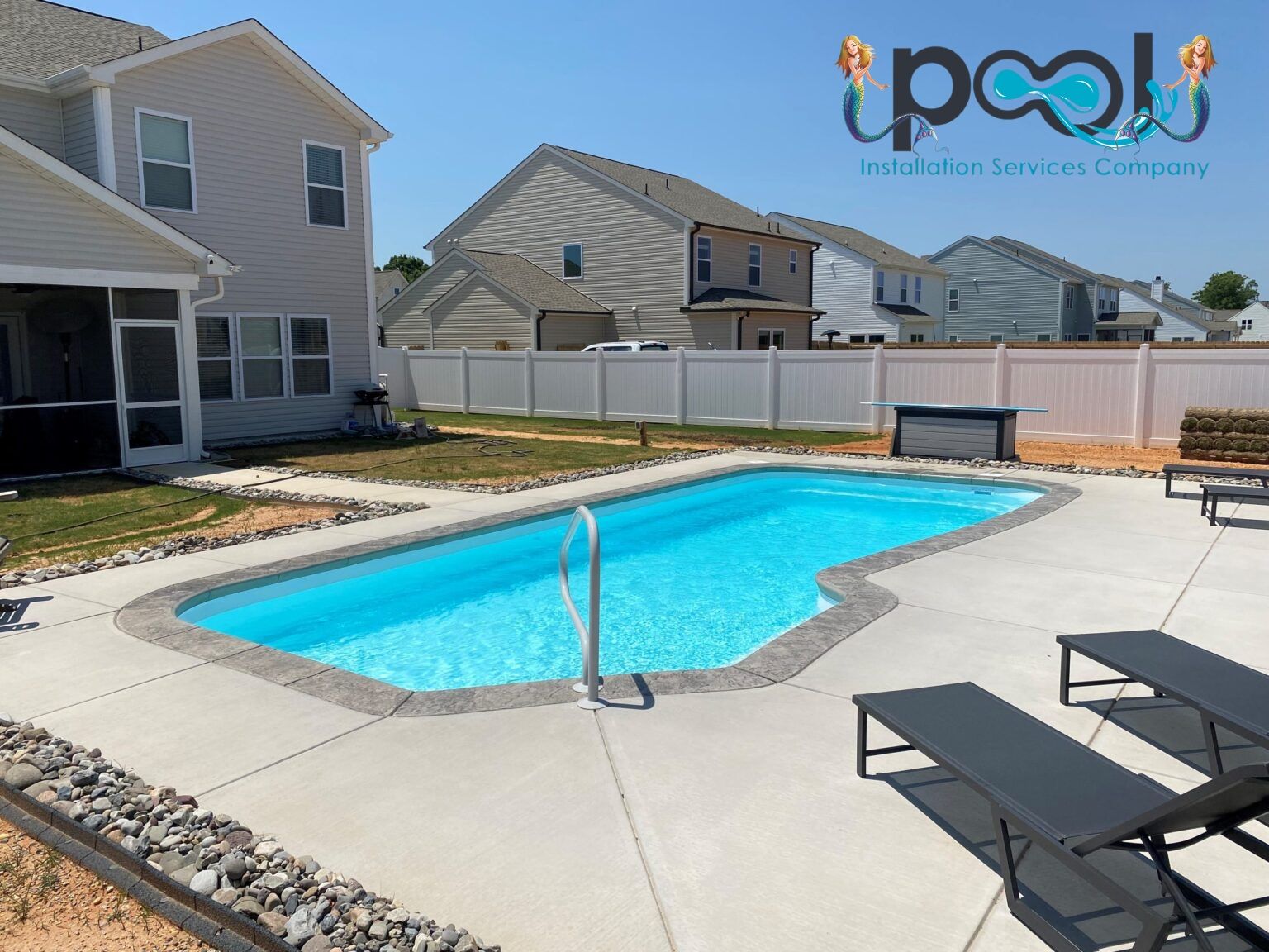 A backyard pool with concrete patio, lounge chairs, and a white fence.