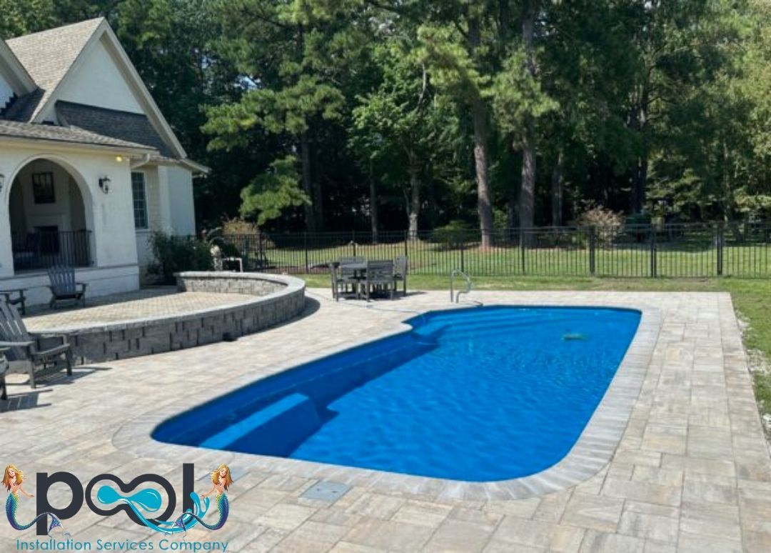 A rectangular swimming pool covered in blue with patio and house in the background.