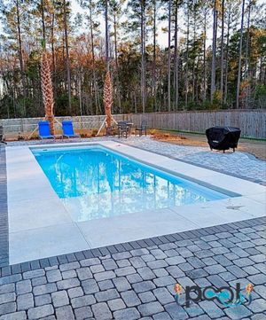 Rectangular pool with blue water and white concrete surround, set on brick patio. Trees in background.