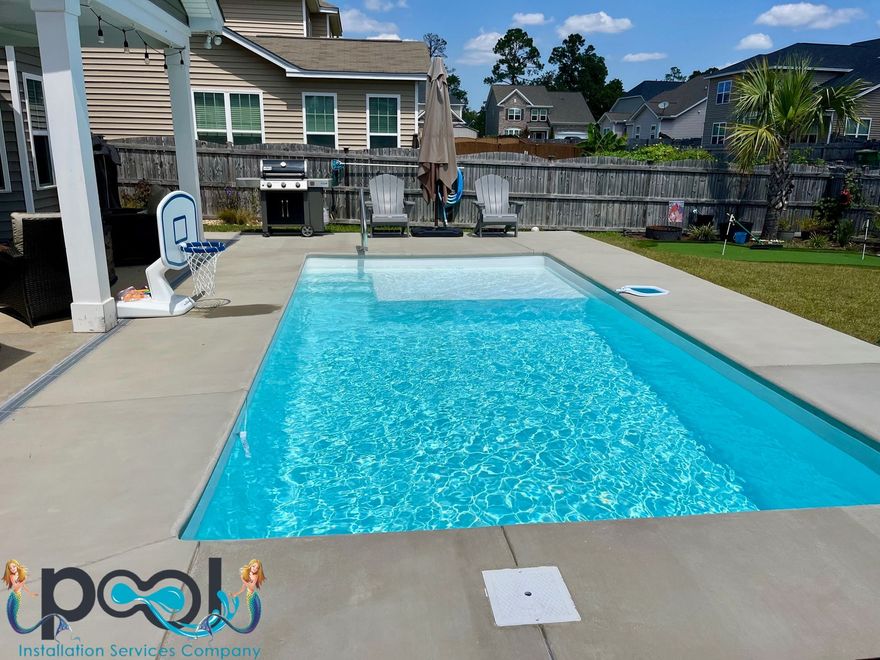 Blue rectangular pool in a backyard with patio, grill, and two chairs. Sunny day.