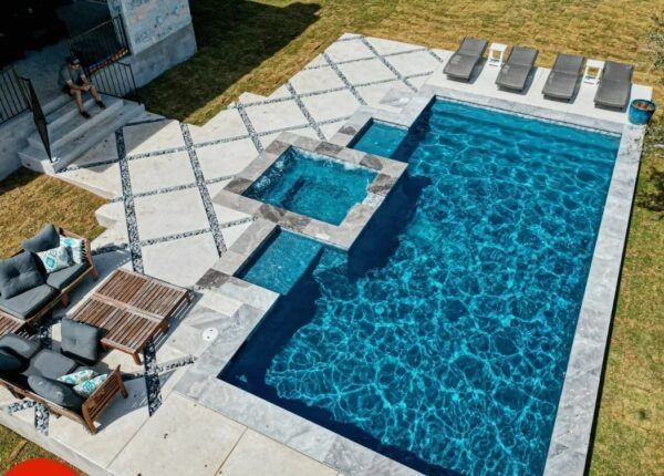 Aerial view of a rectangular swimming pool with a connected jacuzzi and lounge area.