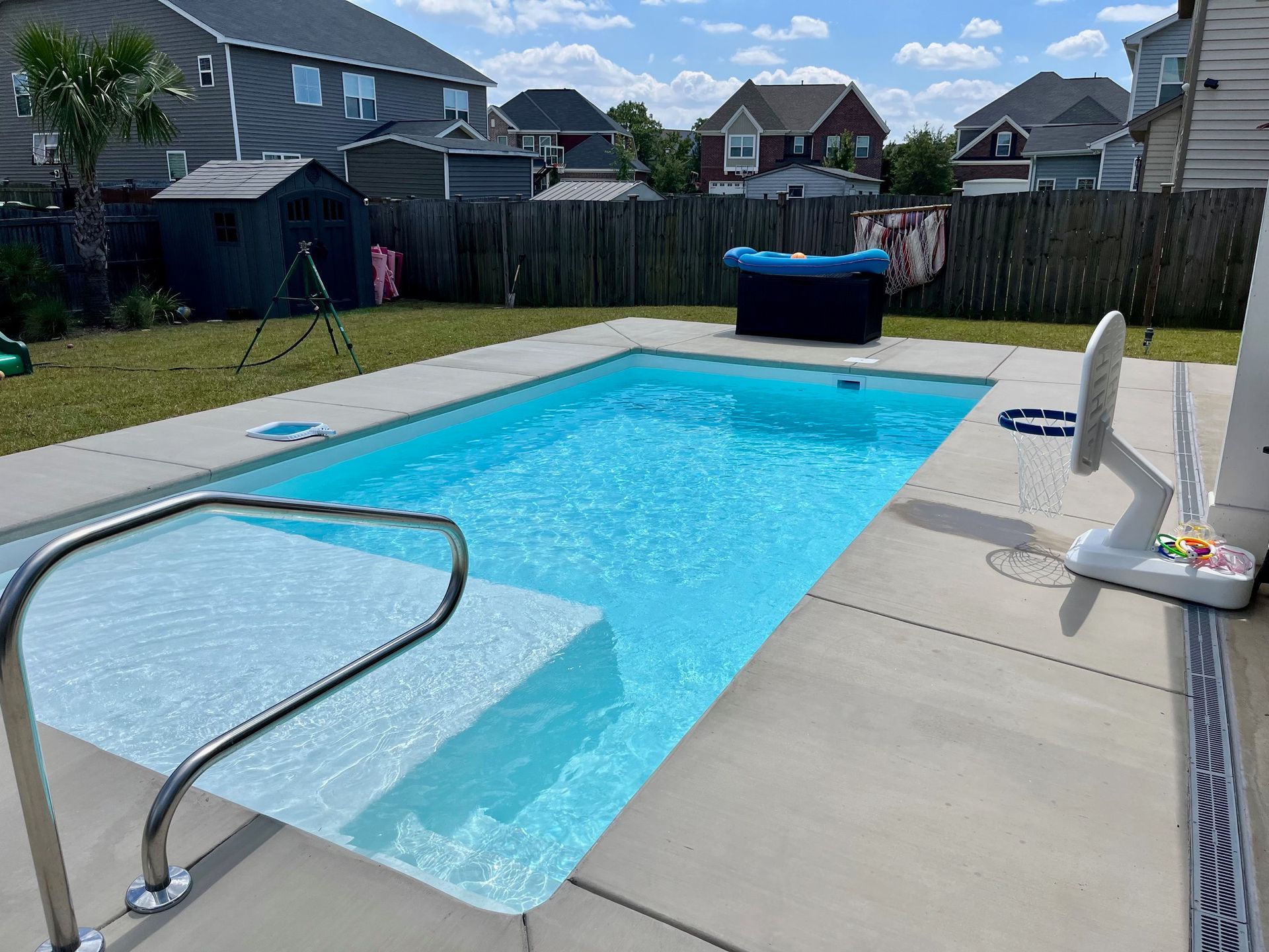 Rectangular backyard pool with steps and a handrail. Sunny day, residential setting.