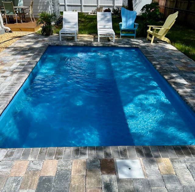 Rectangular pool with blue water, surrounded by brick pavers, and white & yellow chairs.