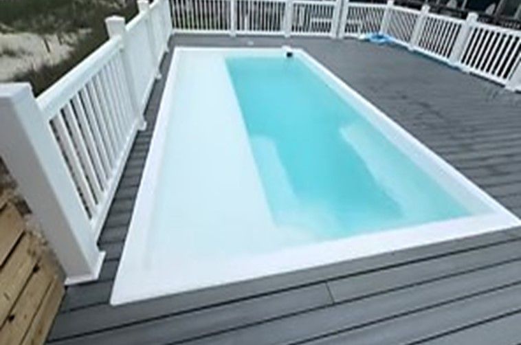 Rectangular above-ground pool on a gray deck with white railing. Turquoise water reflects sunlight.