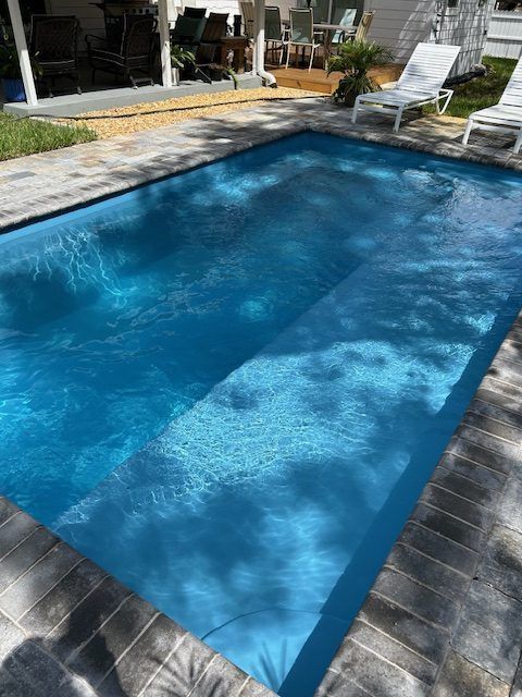 Blue rectangular swimming pool, brick border, sunny outdoor setting.