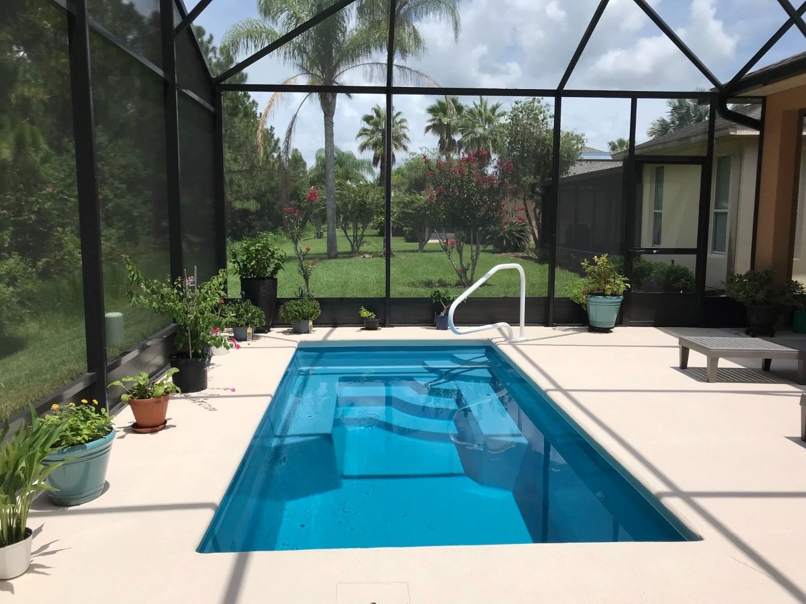 Rectangular pool inside screened enclosure, surrounded by potted plants and a patio.