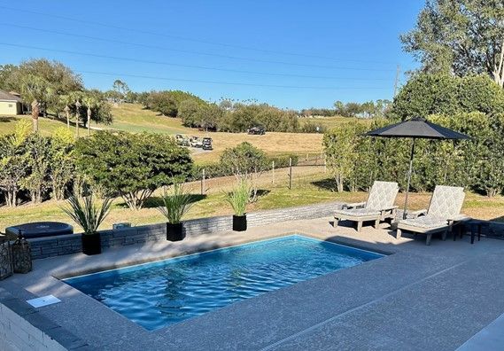 Pool with loungers, overlooking a grassy field under a blue sky.