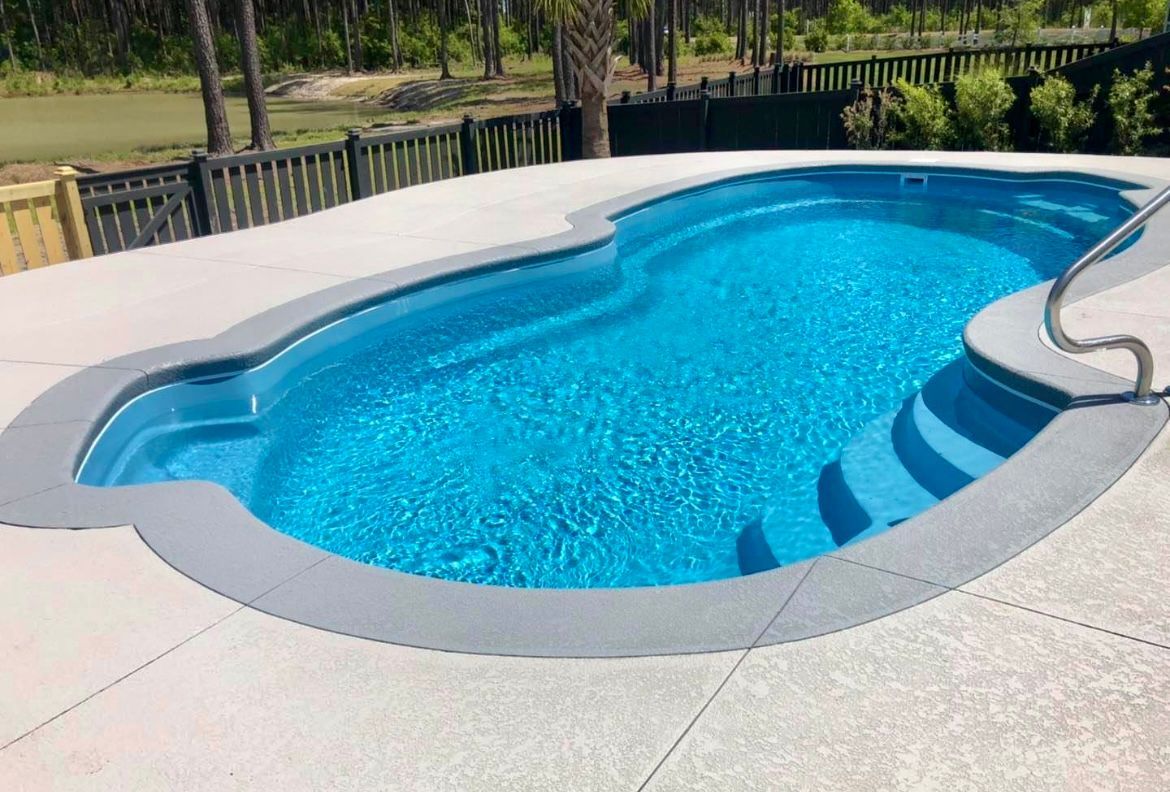 Blue swimming pool with concrete surround in a backyard setting.