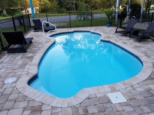 Pool with blue water surrounded by stone pavers and black lounge chairs.
