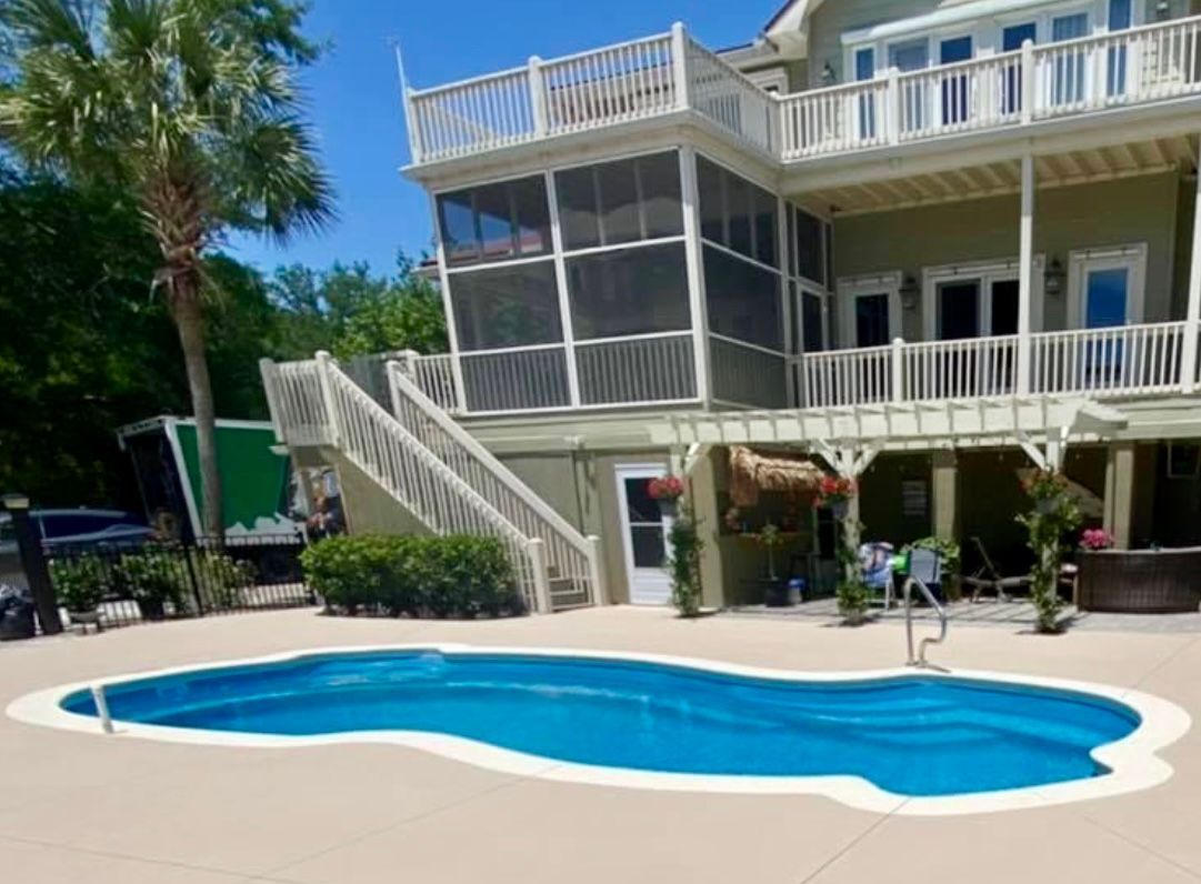 Swimming pool in front of a multi-story house with a screened porch and balconies. Palm tree on the side.