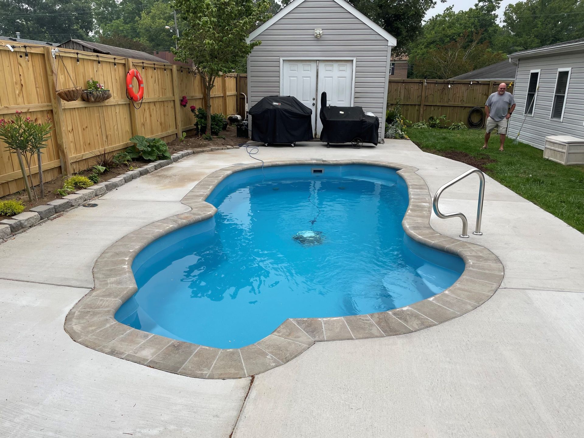 Swimming pool with blue water surrounded by concrete patio. A person walks nearby.