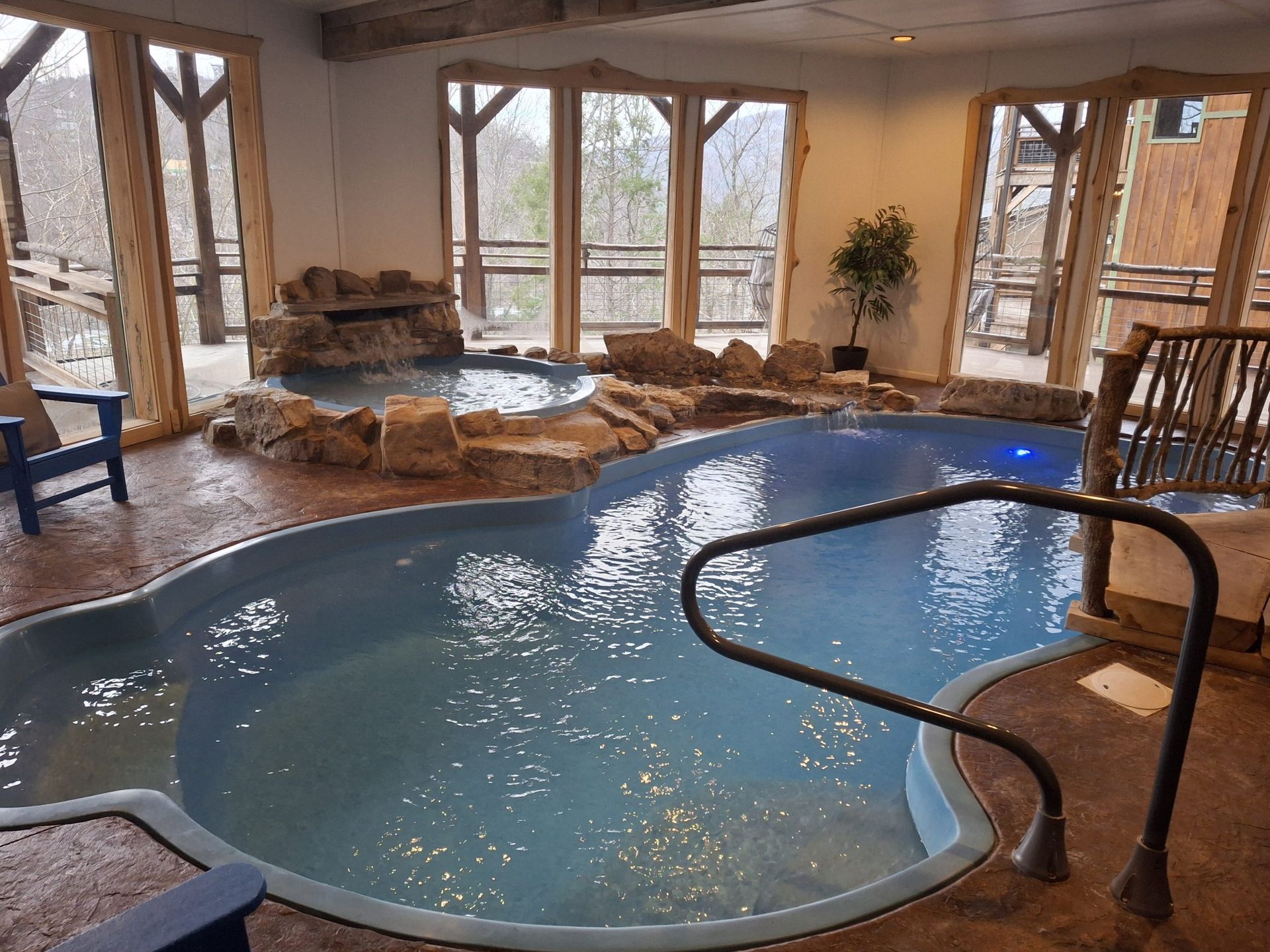 Indoor pool with waterfall feature, surrounded by windows and wood accents. Blue water, rock detail.
