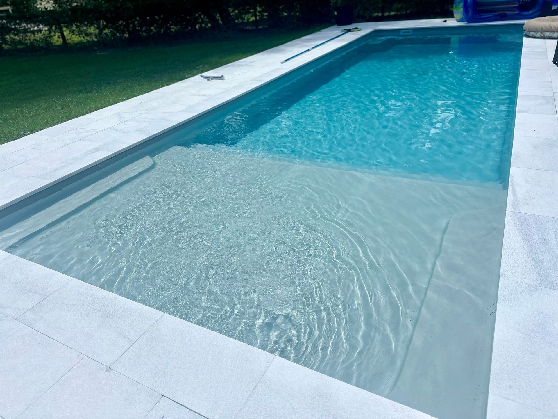 Rectangular pool with shallow and deep ends; light blue water, white tiled deck, and green lawn.