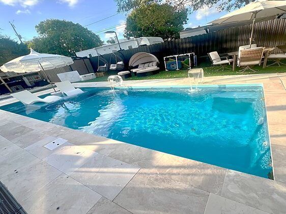 A rectangular pool with fountains, white lounge chairs, and umbrellas in an outdoor setting.
