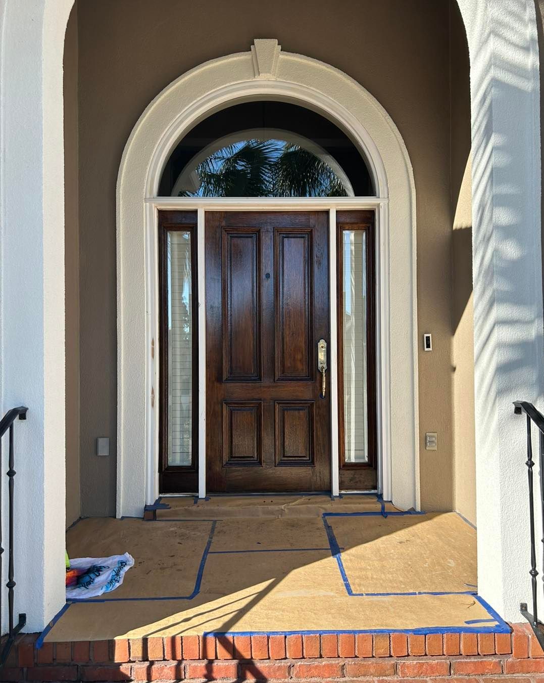 Dark wood front door with side windows, arched top, brown walls, and brick steps.