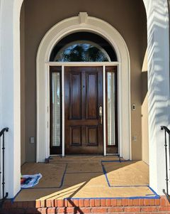 A dark brown wooden front door with sidelights under an arched entrance. The porch is protected with cardboard and tape.