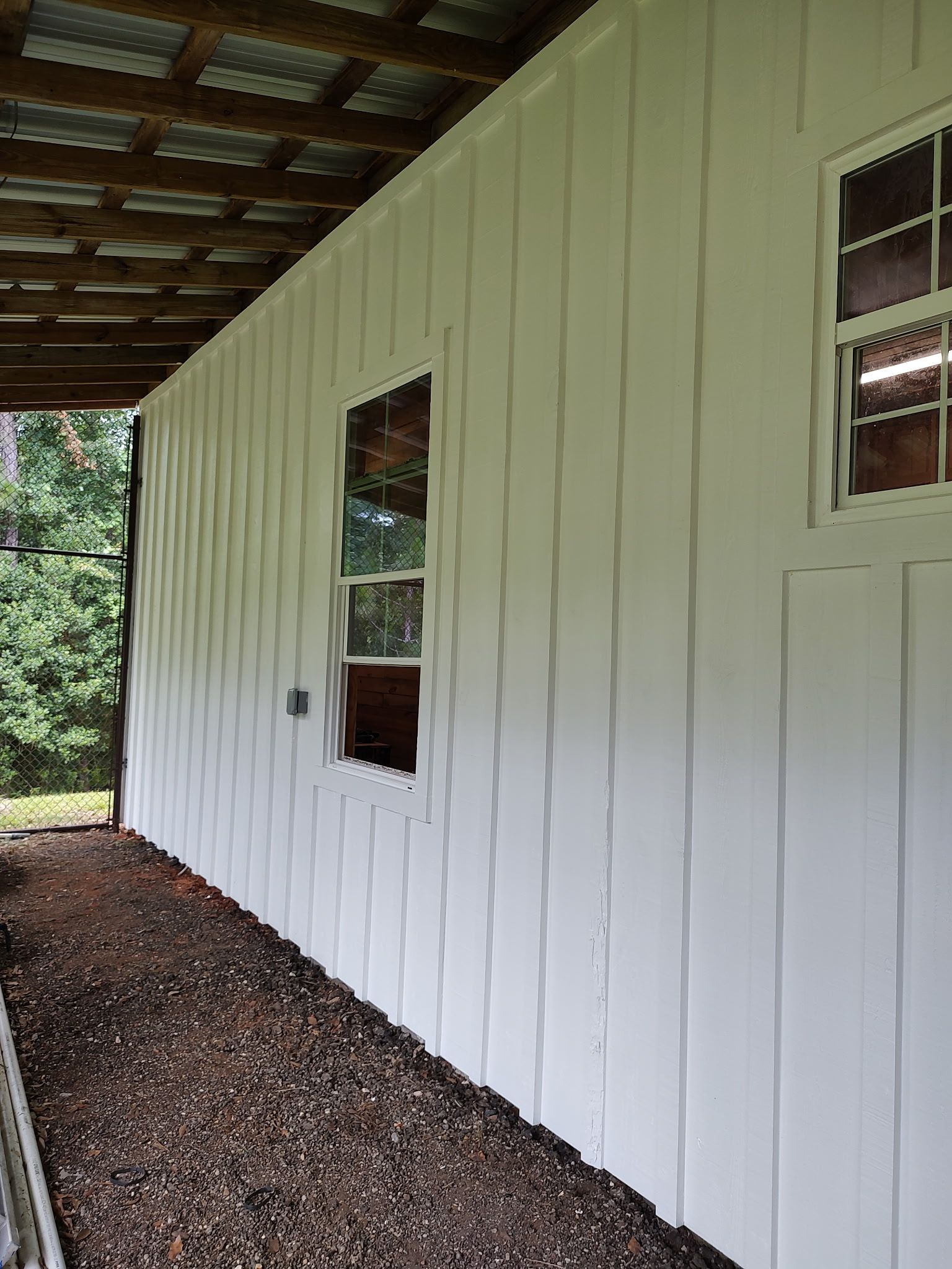 White building with board and batten siding, two windows, and gravel pathway.