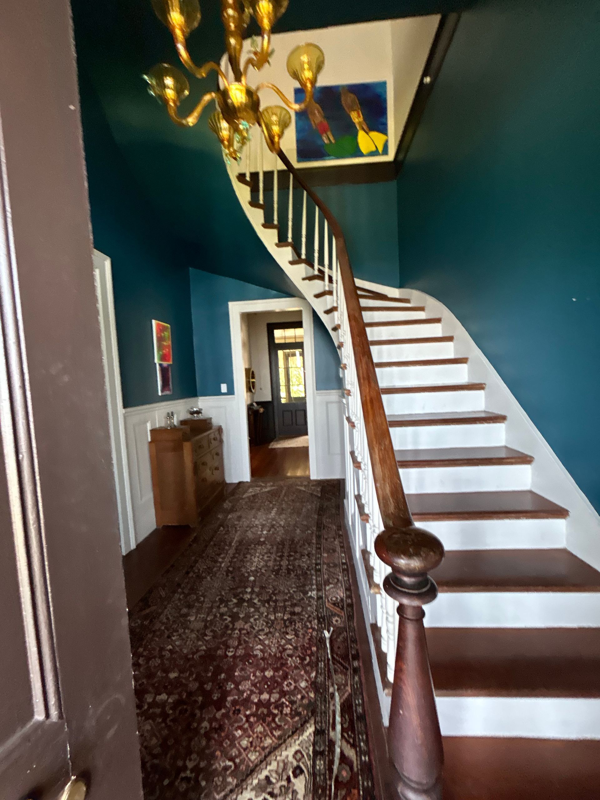 Grand entry hall with teal walls, winding staircase, antique rug, and chandelier.