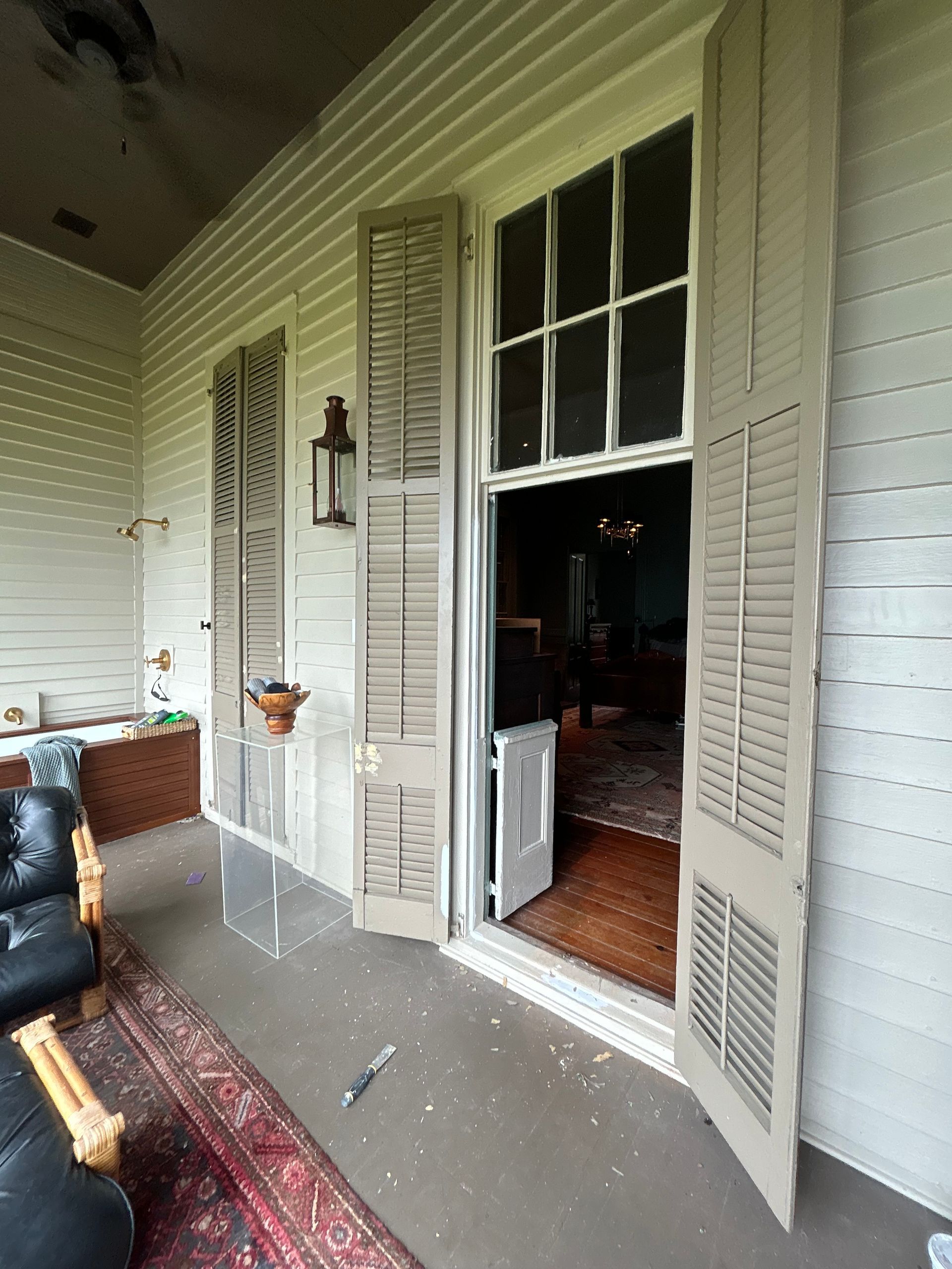Porch with open shutters, revealing a doorway and interior. Creamy white siding and shutters, a rug, and a lantern.
