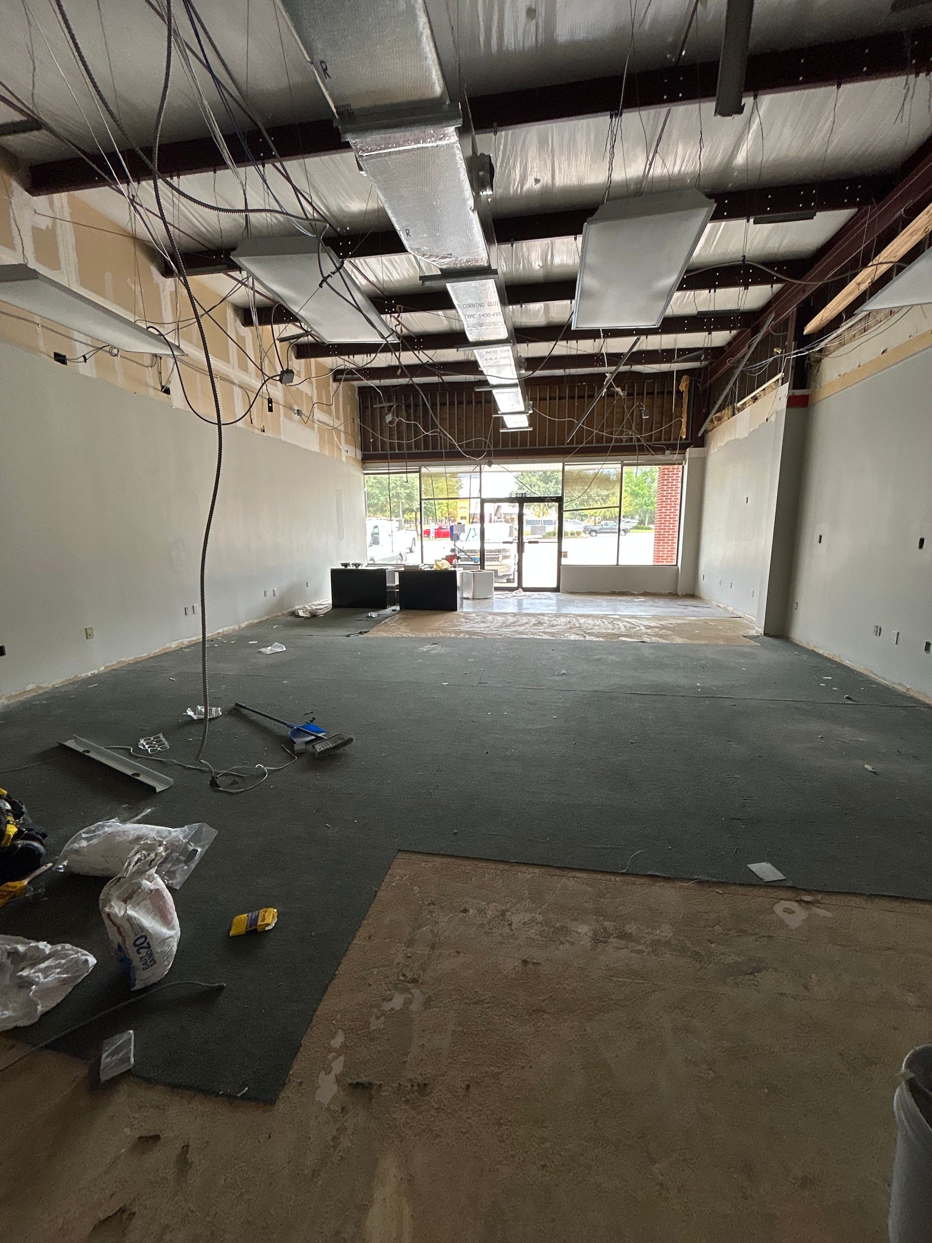 Interior of a commercial space under renovation with exposed ceiling, debris on floor, and front door visible.