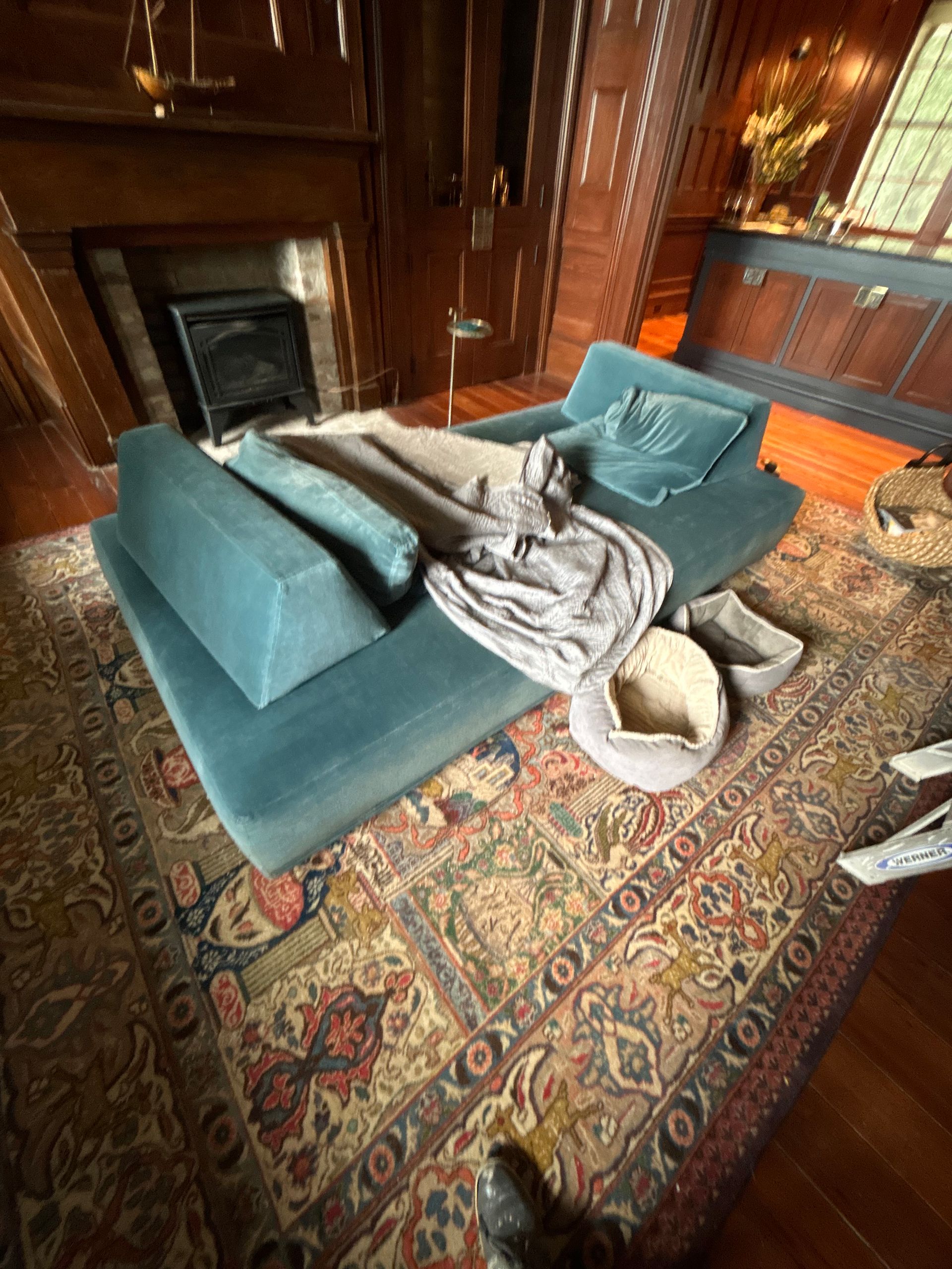 Teal chaise lounge on patterned rug, in a room with dark wood paneling and fireplace.