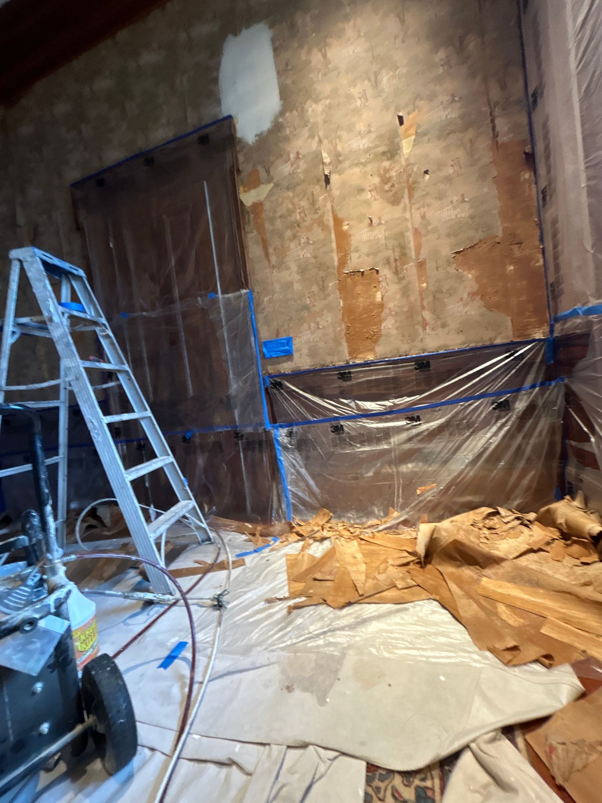 Construction site: wall covered in plastic, ladder, paint sprayer, debris on floor.