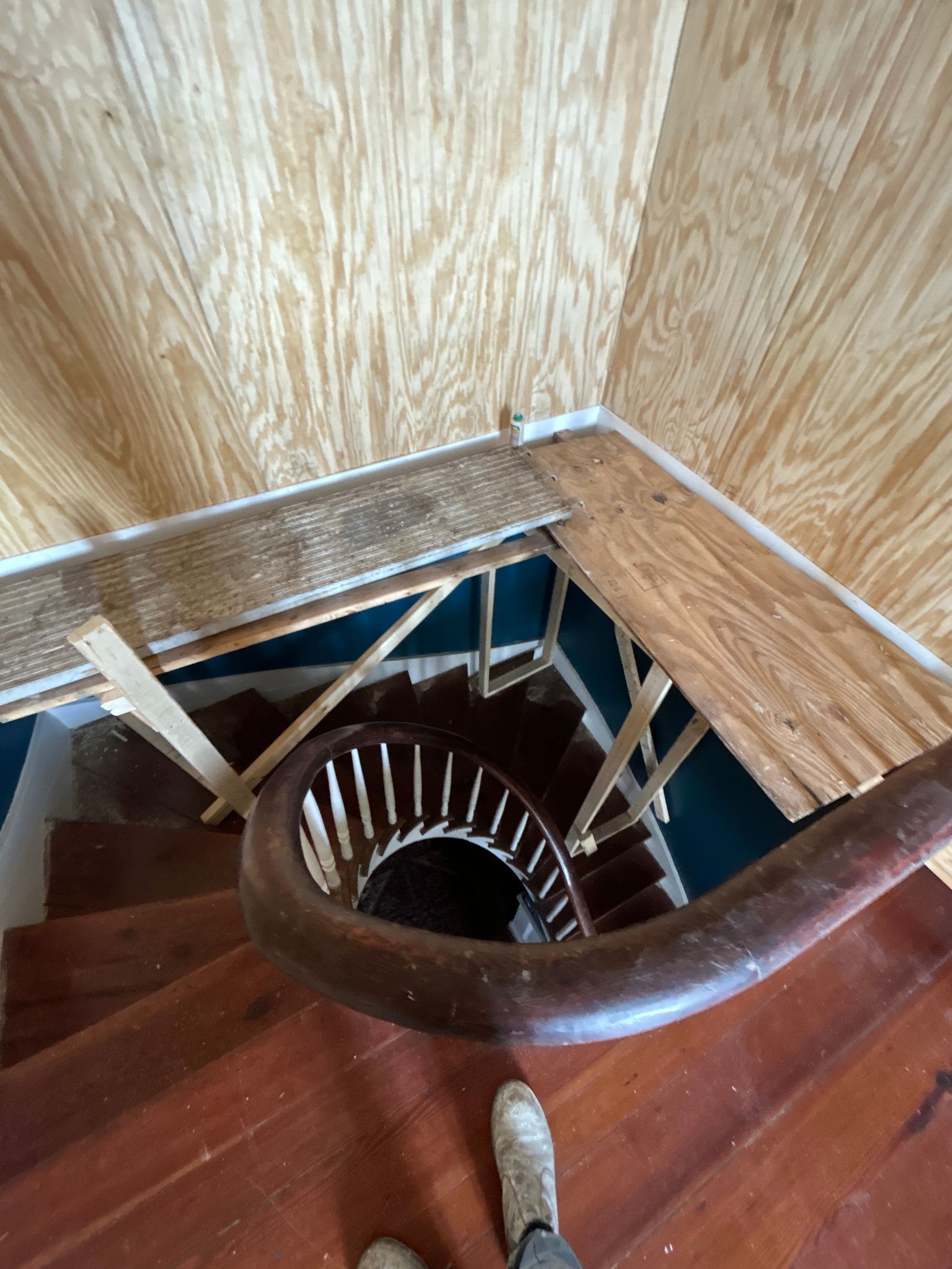 Top-down view of spiral staircase with dark wooden steps, brown railing, and light wood walls.