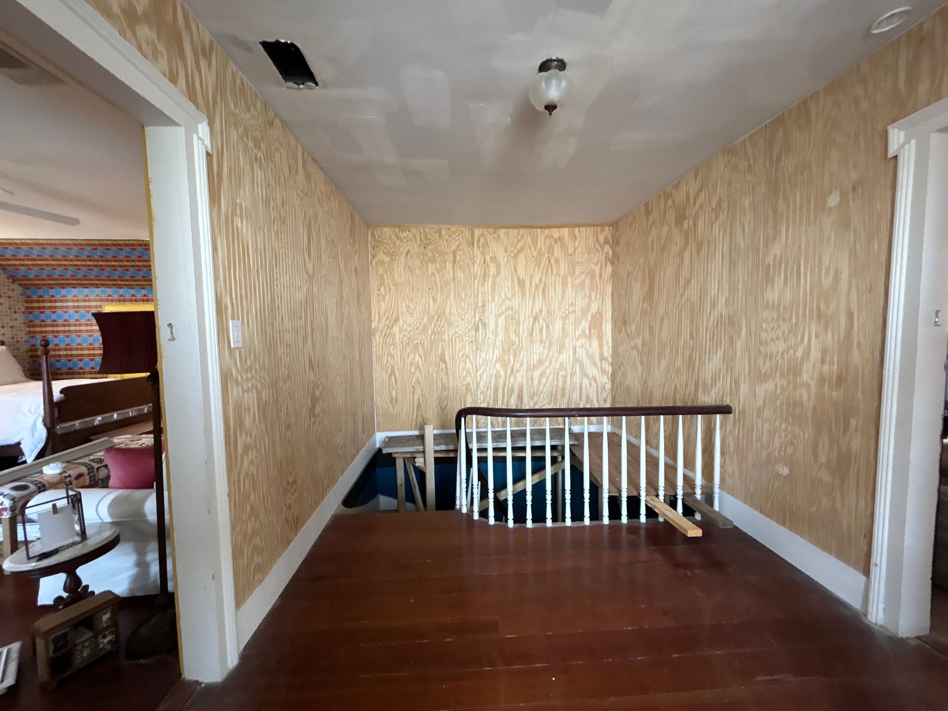 Hallway with wood floor and walls. Staircase with white railing leads down. Beige wallpaper.
