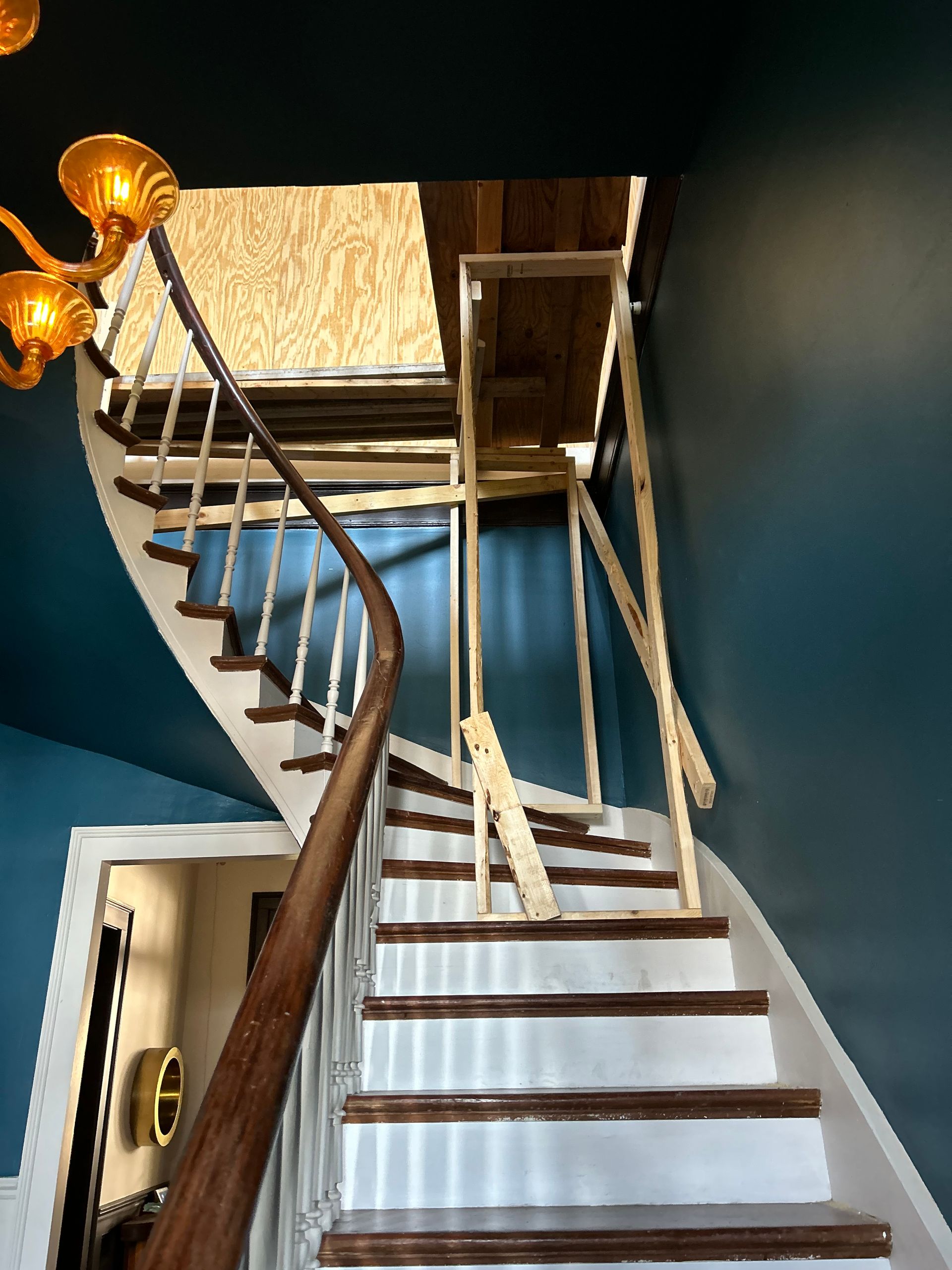 Curved staircase leading upwards. Temporary wooden supports extend to the attic. Teal walls.
