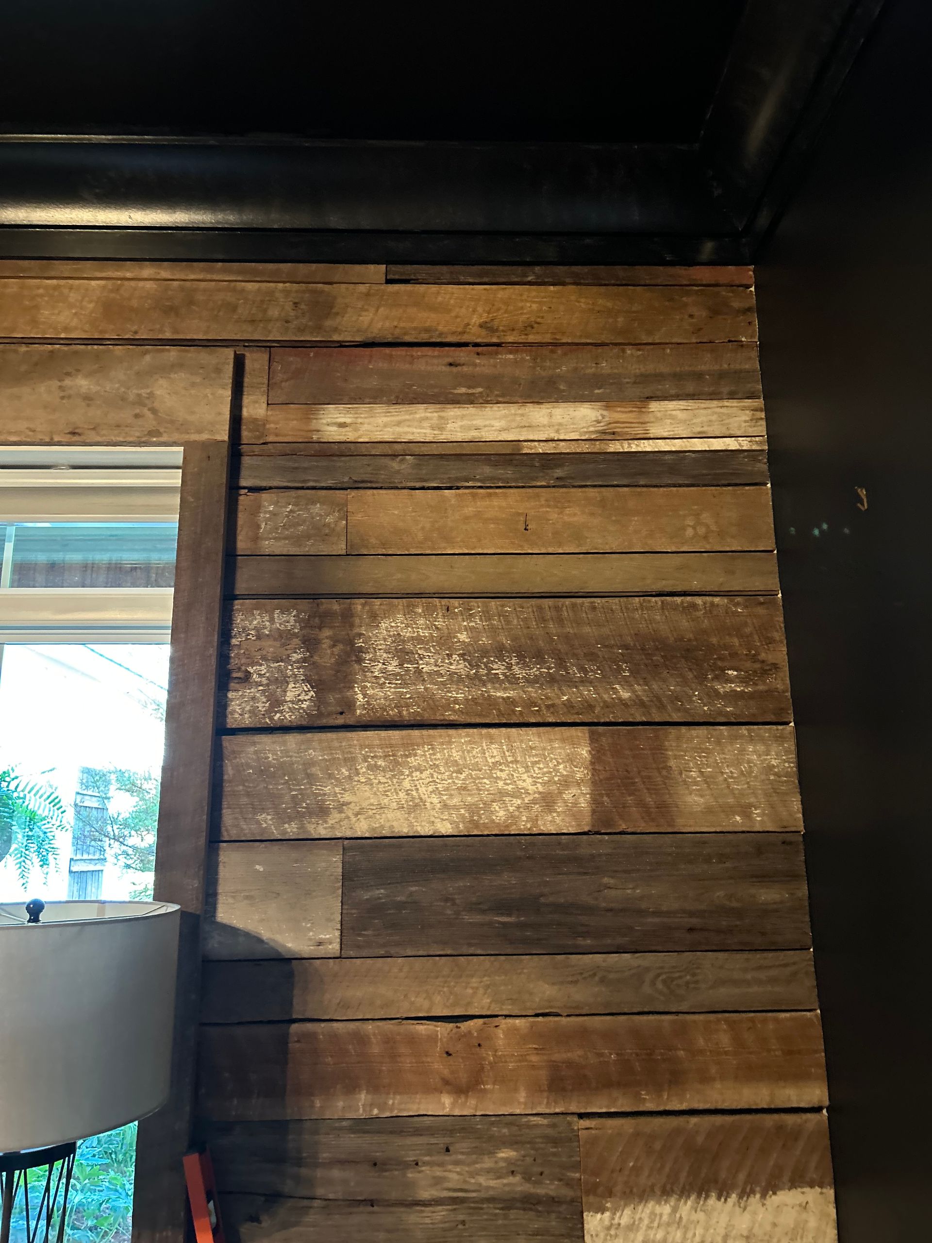 Wooden wall paneling with various shades of brown and gray. A window is on the left, black wall on the right.