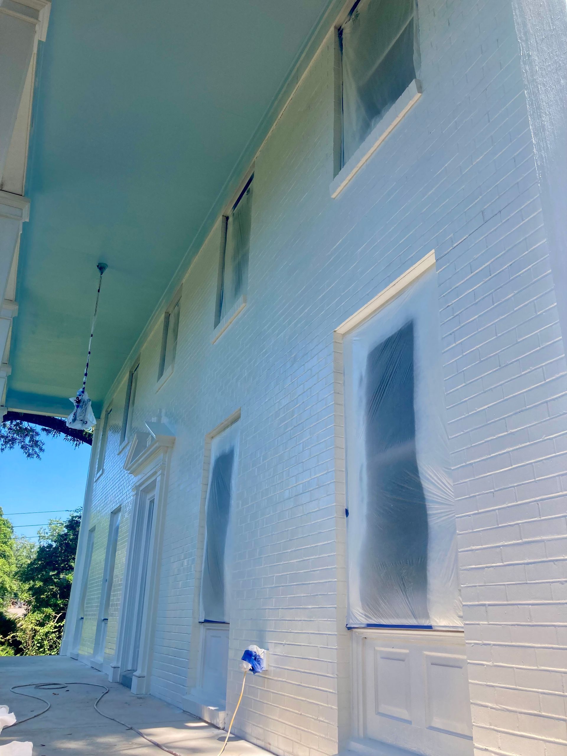 White painted brick building with blue ceiling, windows masked for painting.