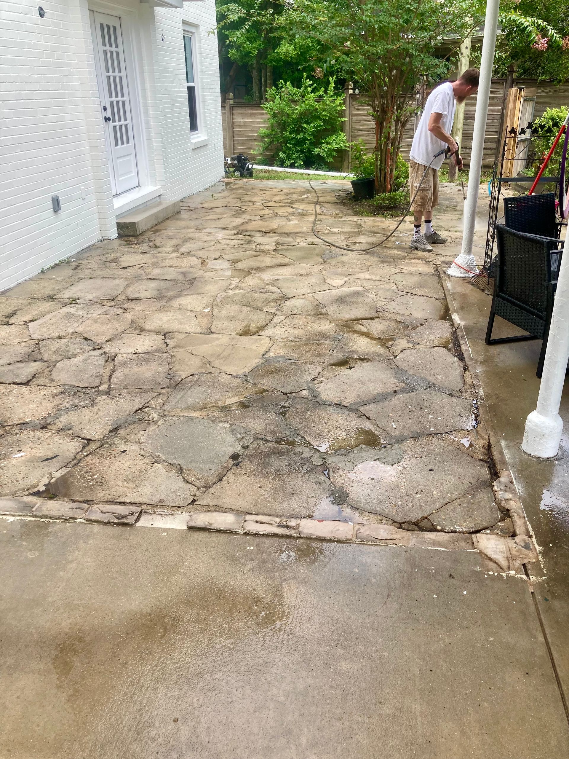 Man power washing a stone patio next to a white building with a door.