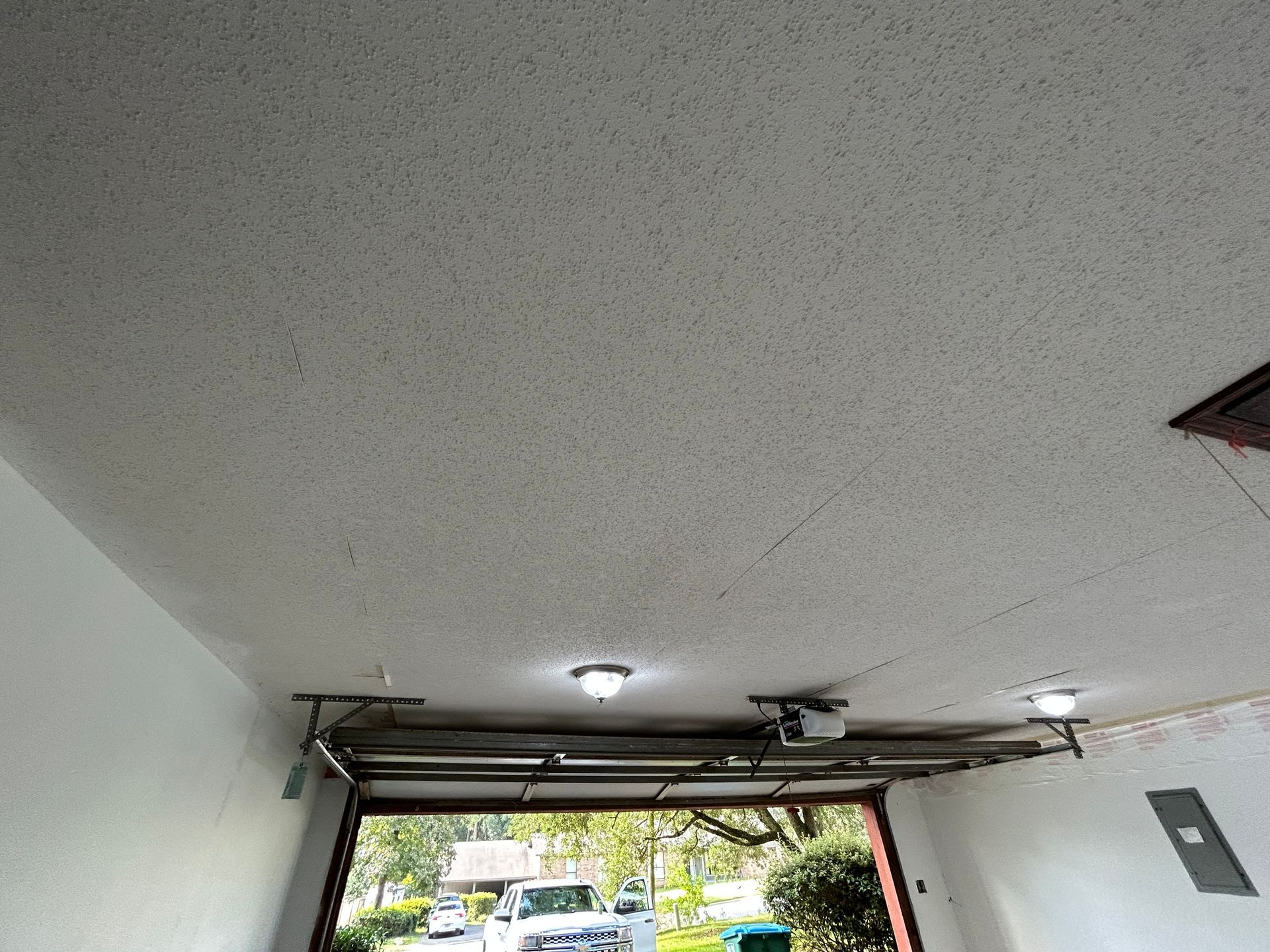 Garage ceiling with textured surface, open door, and car visible outside. Two lights are mounted.