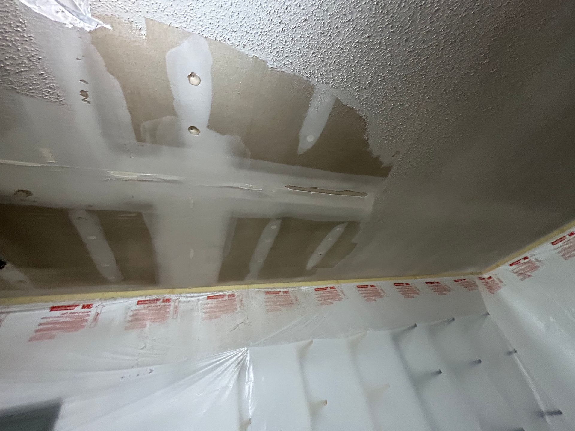 Water-damaged ceiling with peeling paint and plastic sheeting covering the walls, indicating repair work.