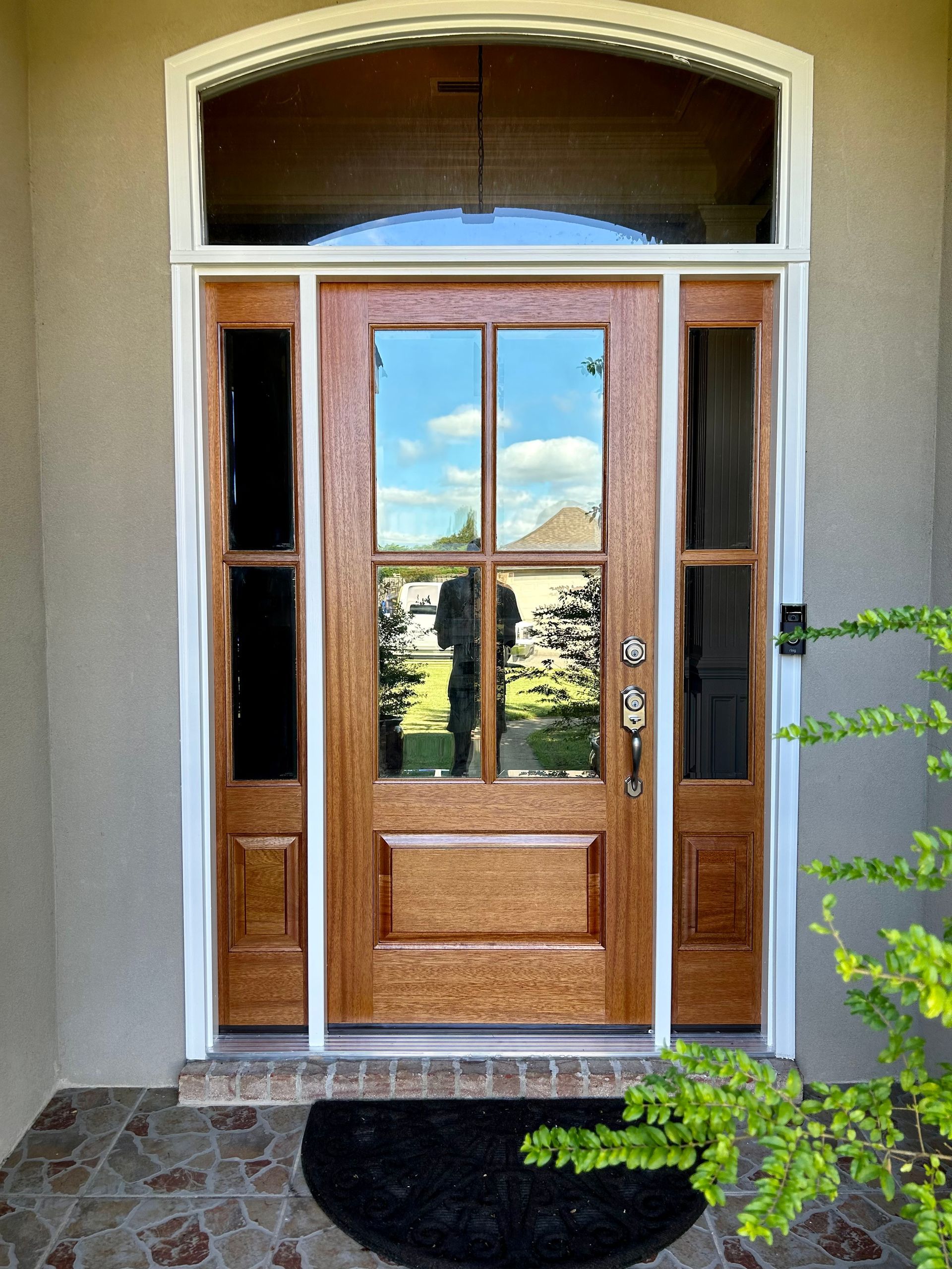 Wooden front door with glass panels, flanked by sidelights, beneath an arched transom.