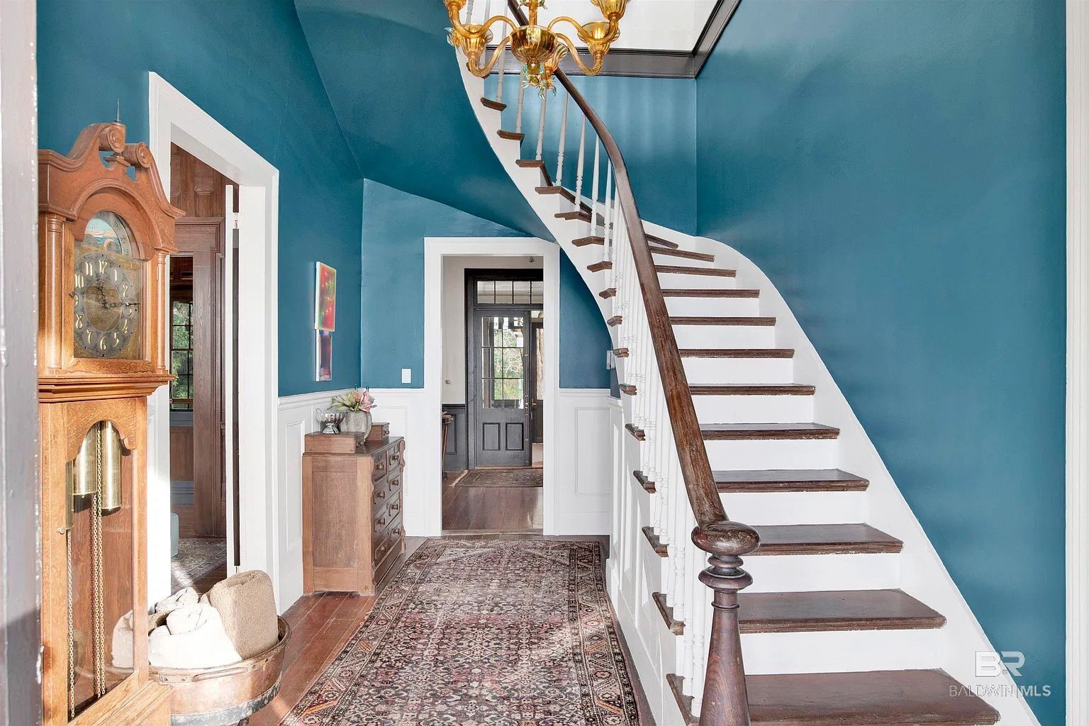 Entryway with teal walls, curved staircase, grandfather clock, and ornate rug.
