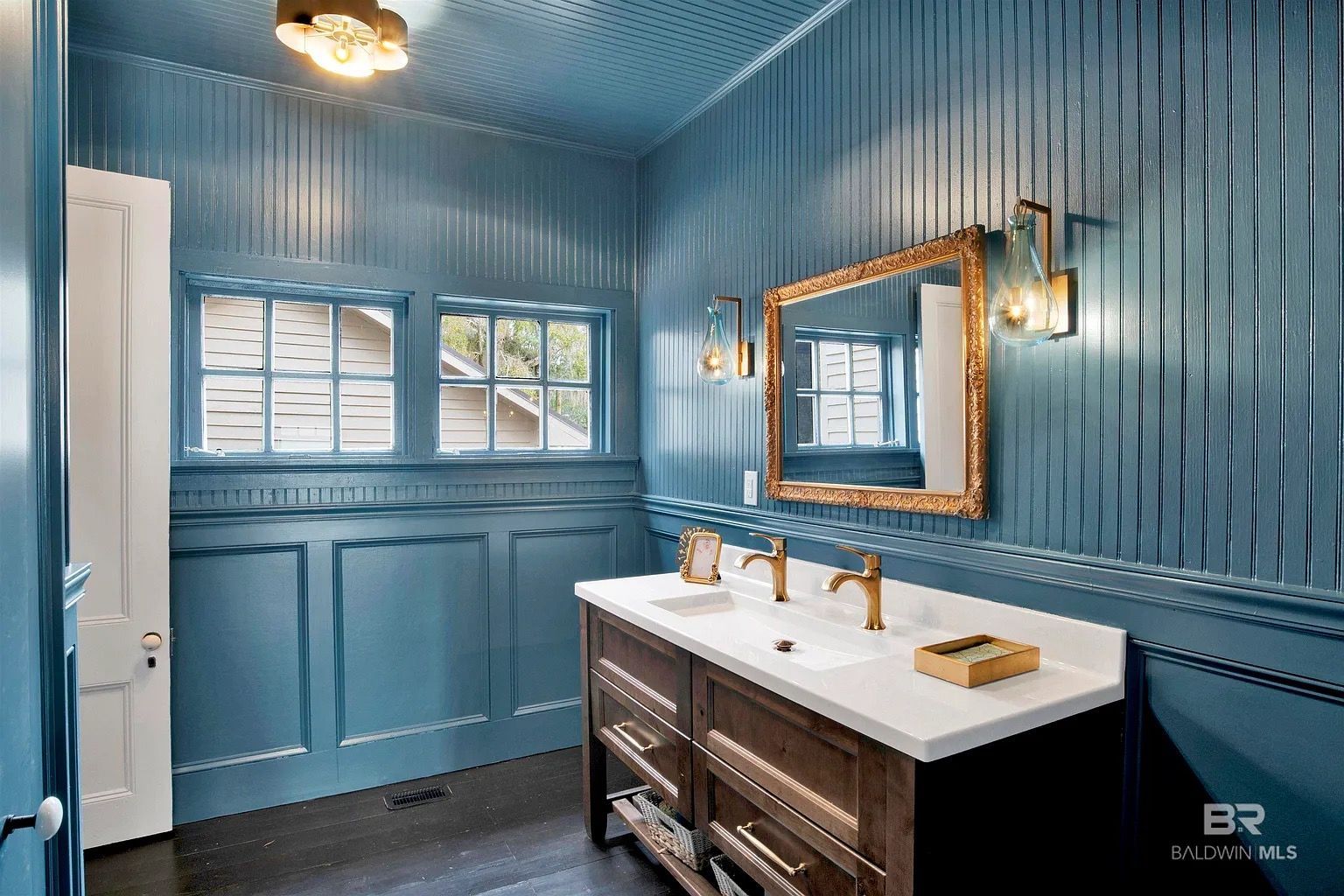 Blue bathroom with wood vanity, gold mirror, and sconces.