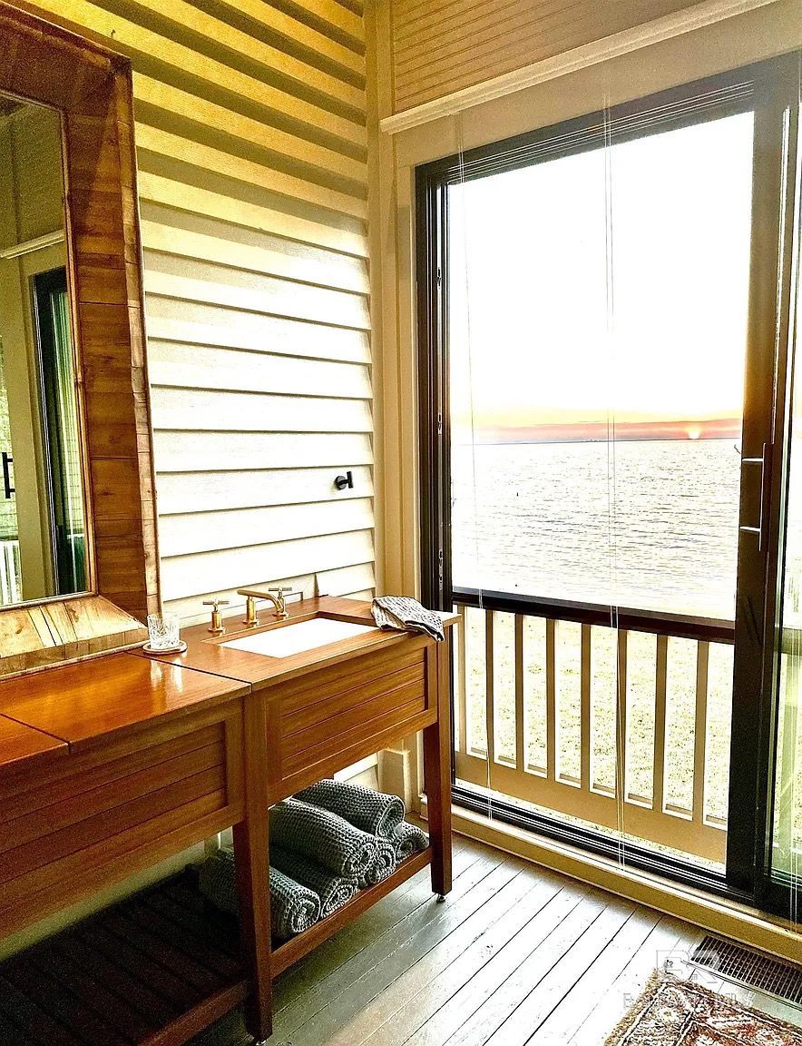 Wooden bathroom with a vanity, mirror, and a view through a screen door to the outdoors.