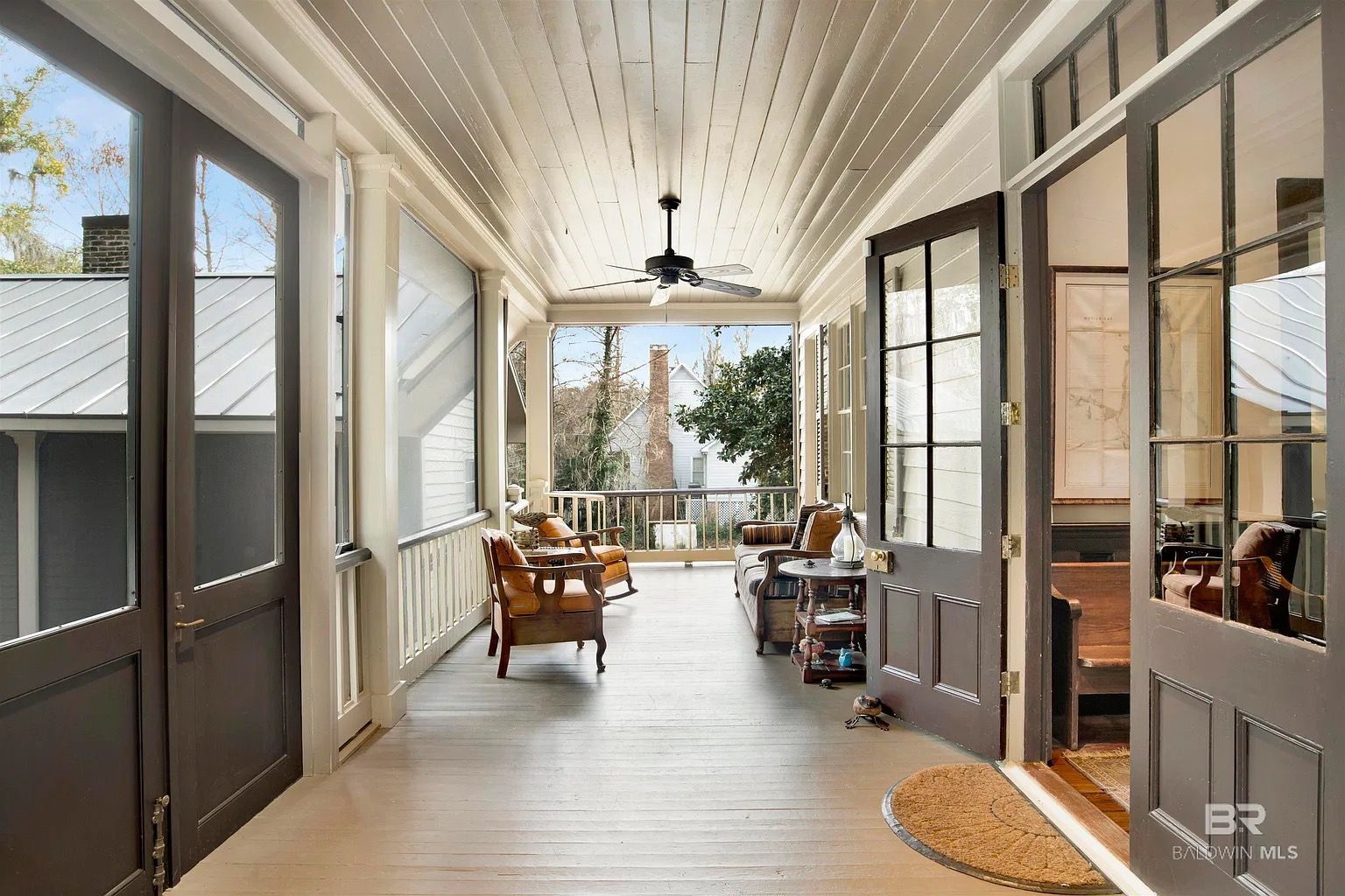 A long, enclosed porch with seating, painted gray and white, with doors open to the inside and outside.