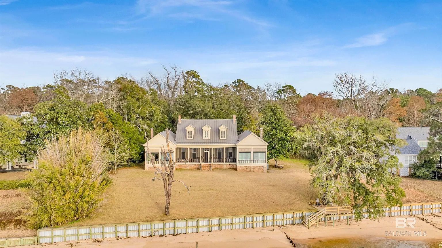 A house with a screened porch, three dormers, and a view of the water. Blue sky with trees.