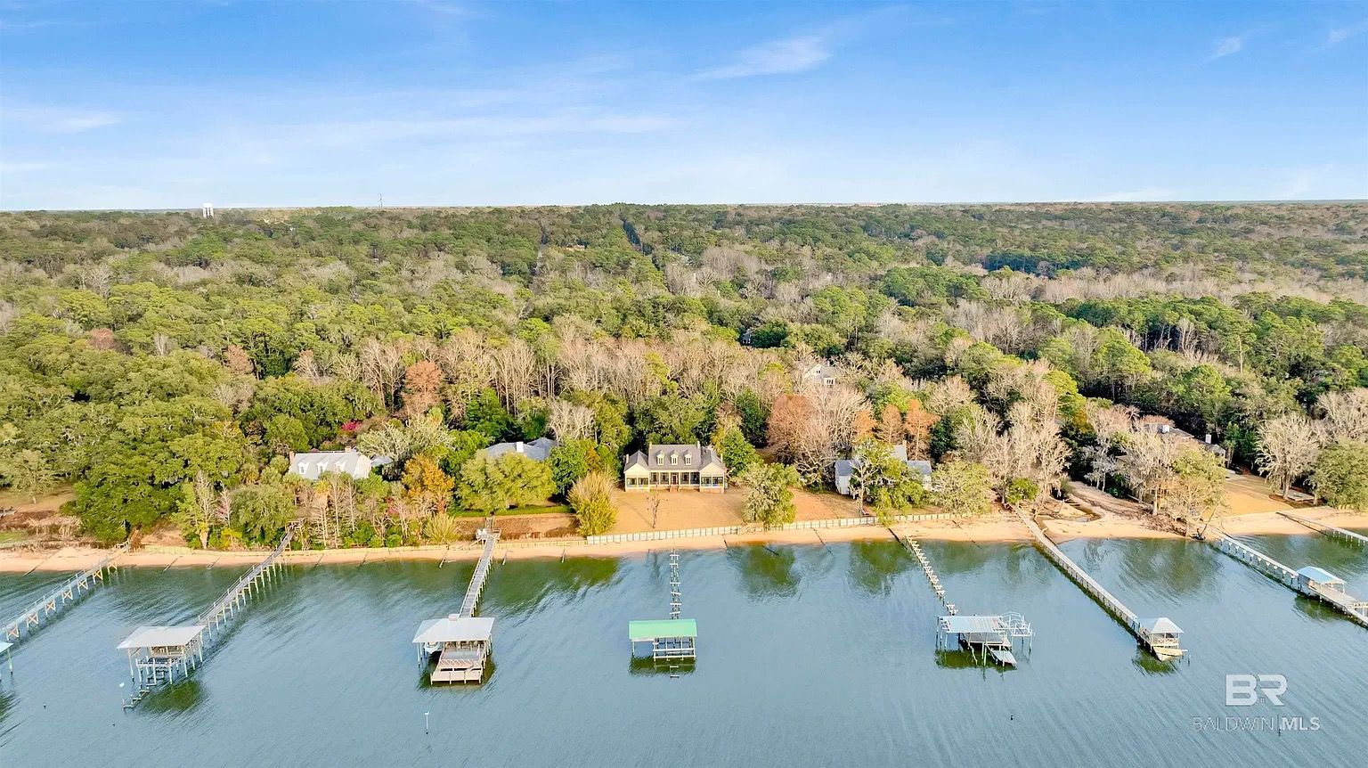 Houses on a lake with docks. Green trees in the background under a blue sky.