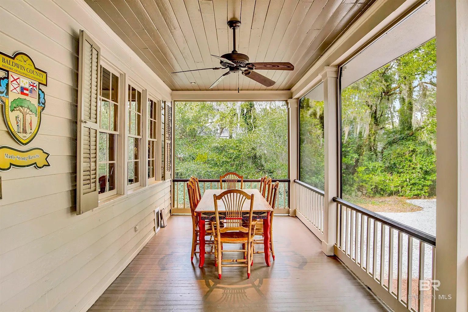 Covered porch with dining table, surrounded by windows, overlooking a lush, green landscape.