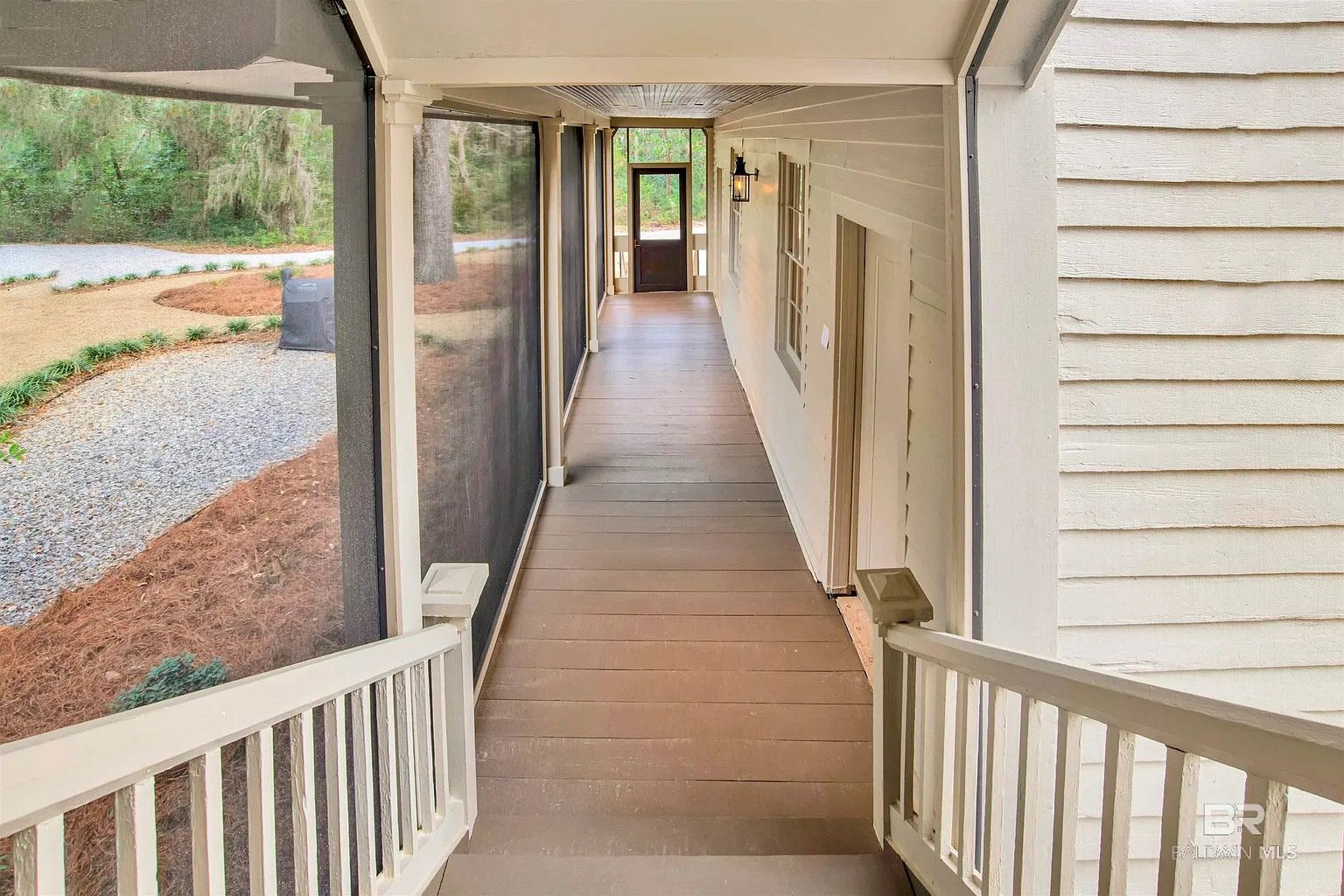 Wooden porch with screened walls and a door at the end, overlooking a landscaped area.