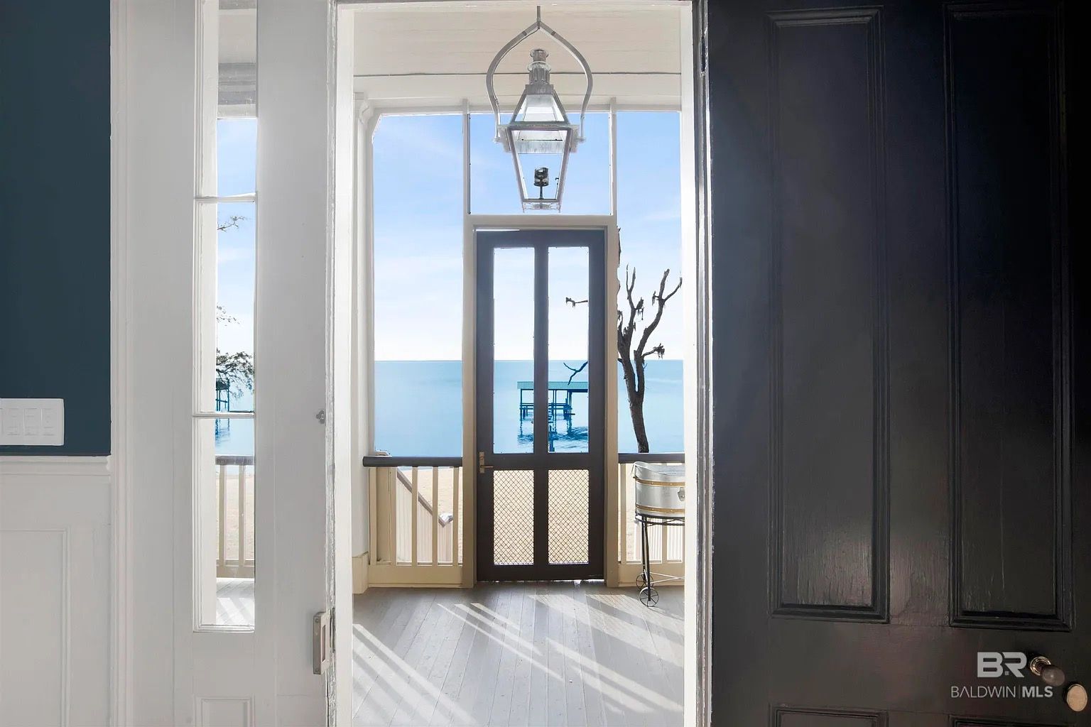 Open door view to the sea; a room with blue, white, and dark wood doors.