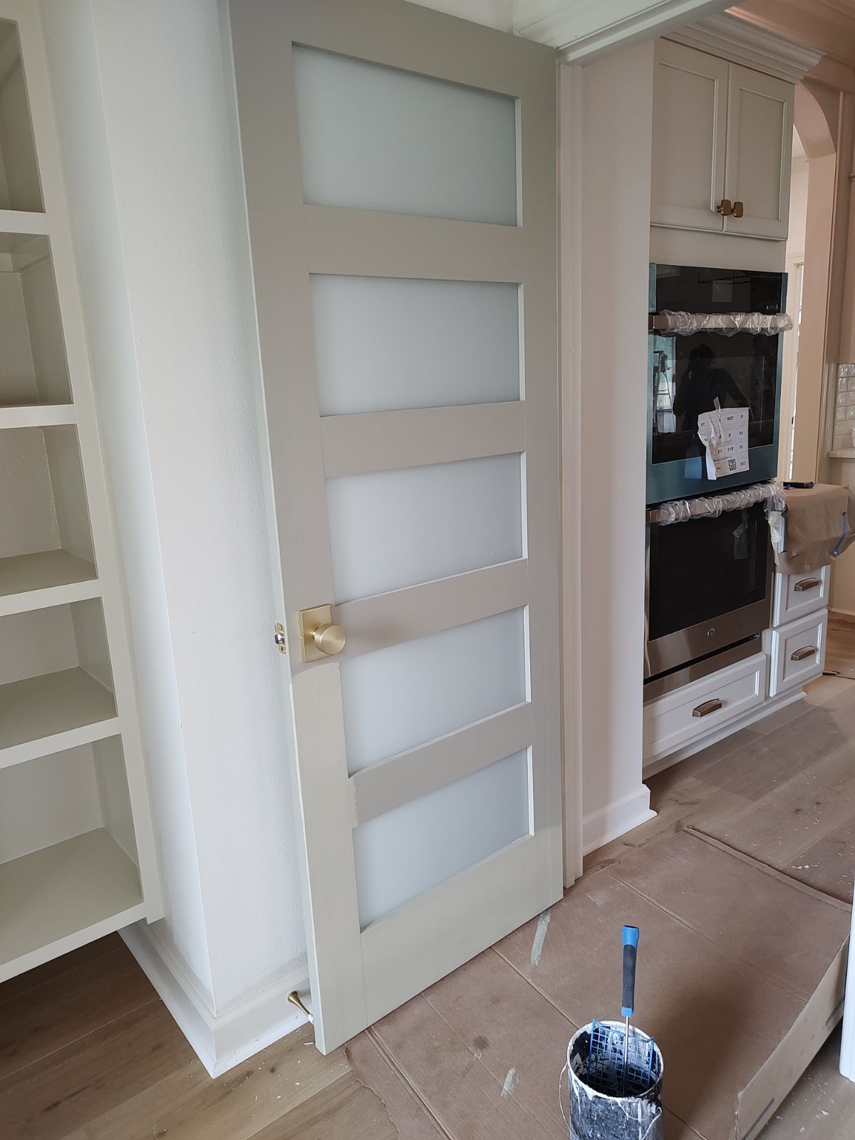 Light gray interior door with frosted glass panels, gold hardware, and white trim in a kitchen.
