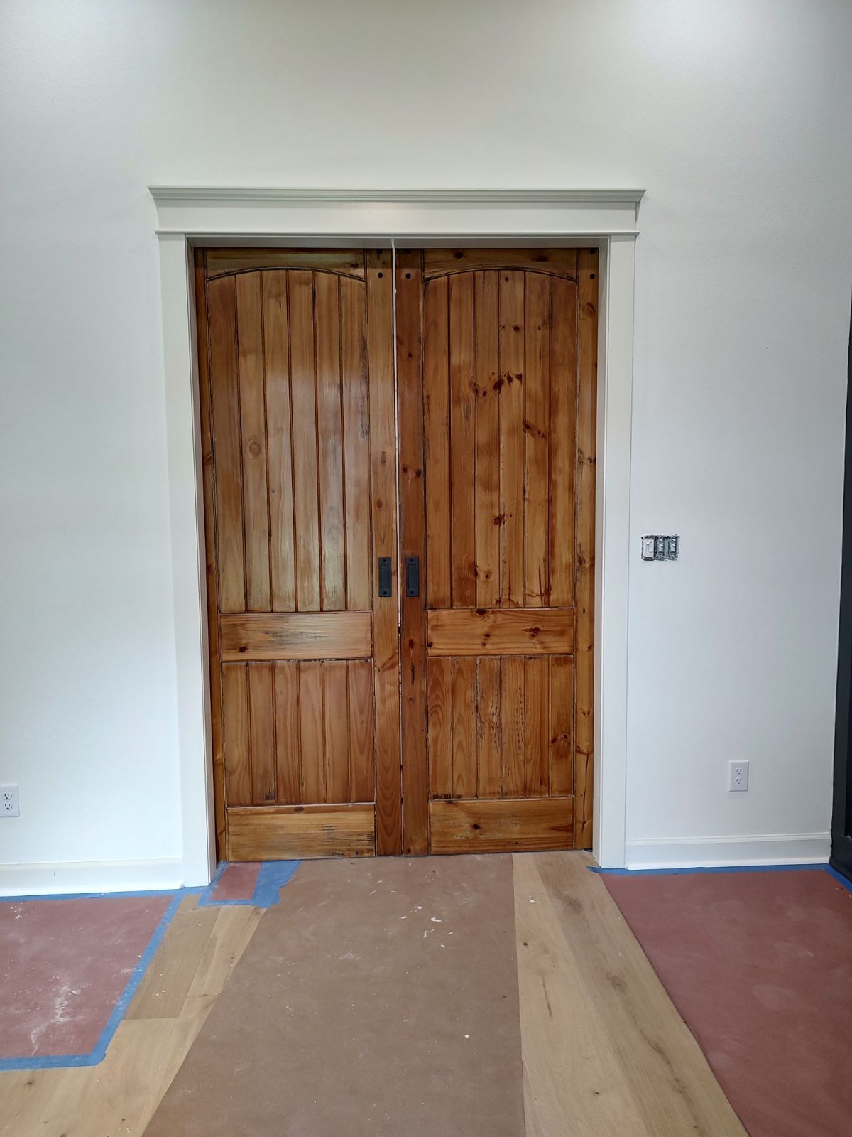 Wooden double doors in a white-walled room, framed with white trim. Brown wood floor in the foreground.