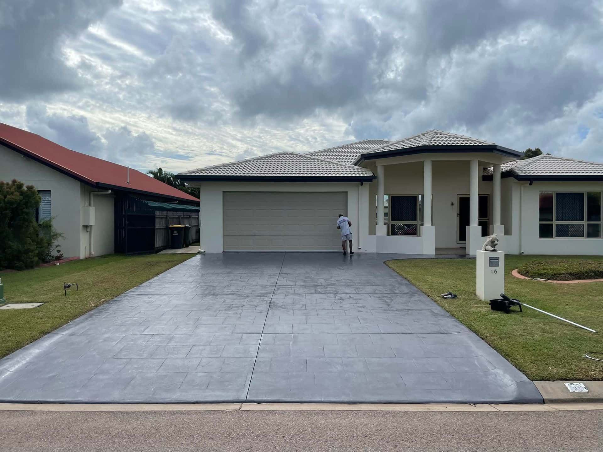 A man is standing in front of a house with a concrete driveway.